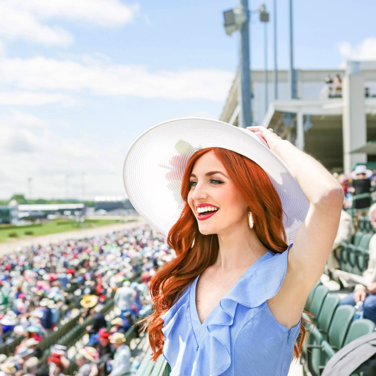 A red-headed woman in Derby hat and attire in the stands of Churchill Downs